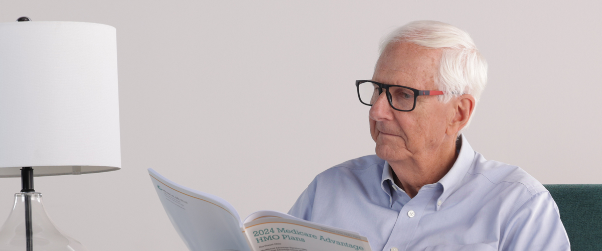 Senior man wearing glasses reading a Medical Mutual brochure.