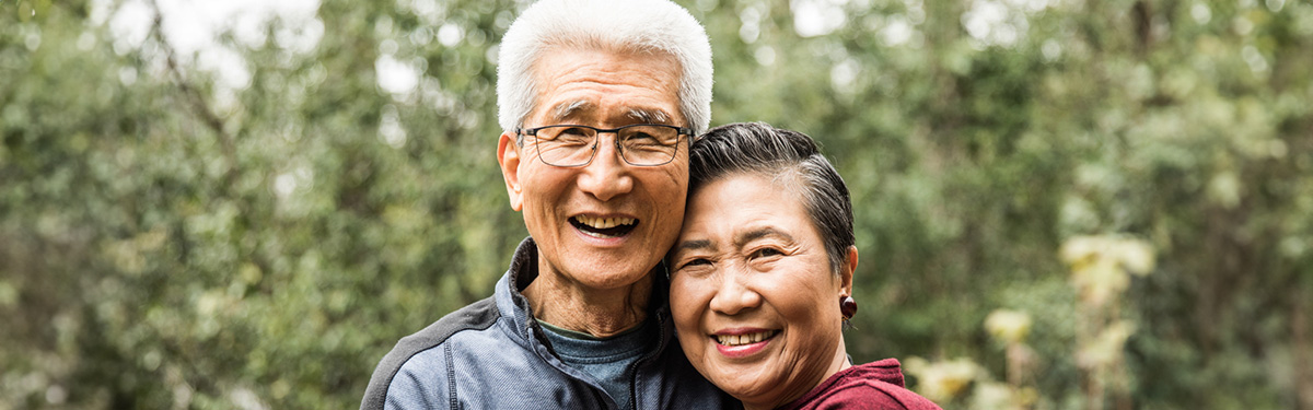 An older couple hugging, posing for a photo outdoors.