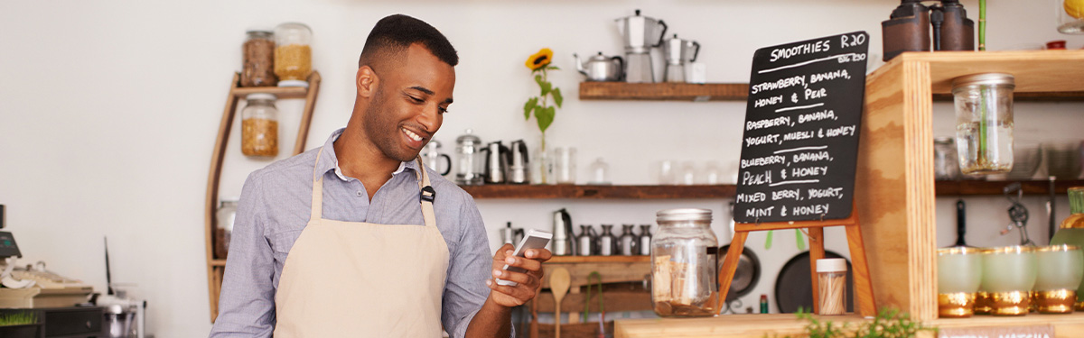 Man working at a coffee shop looking at his cell phone.