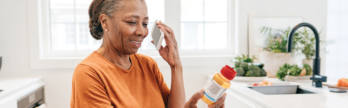 Woman talking on the phone in her kitchen, reading the label of a prescription medication bottle.