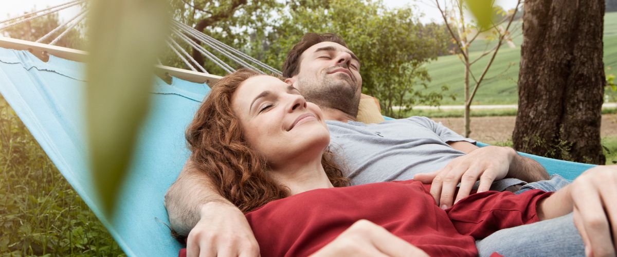 A man and woman resting on an outdoor hammock.